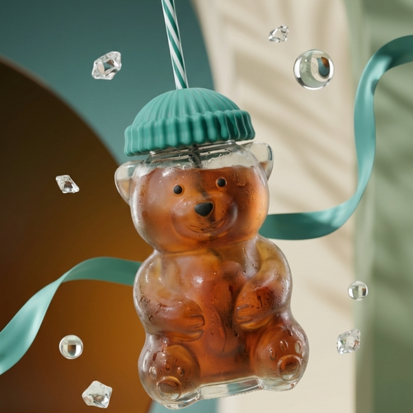 Teddy bear-shaped drink with a green straw and teal ribbon on a blurred background