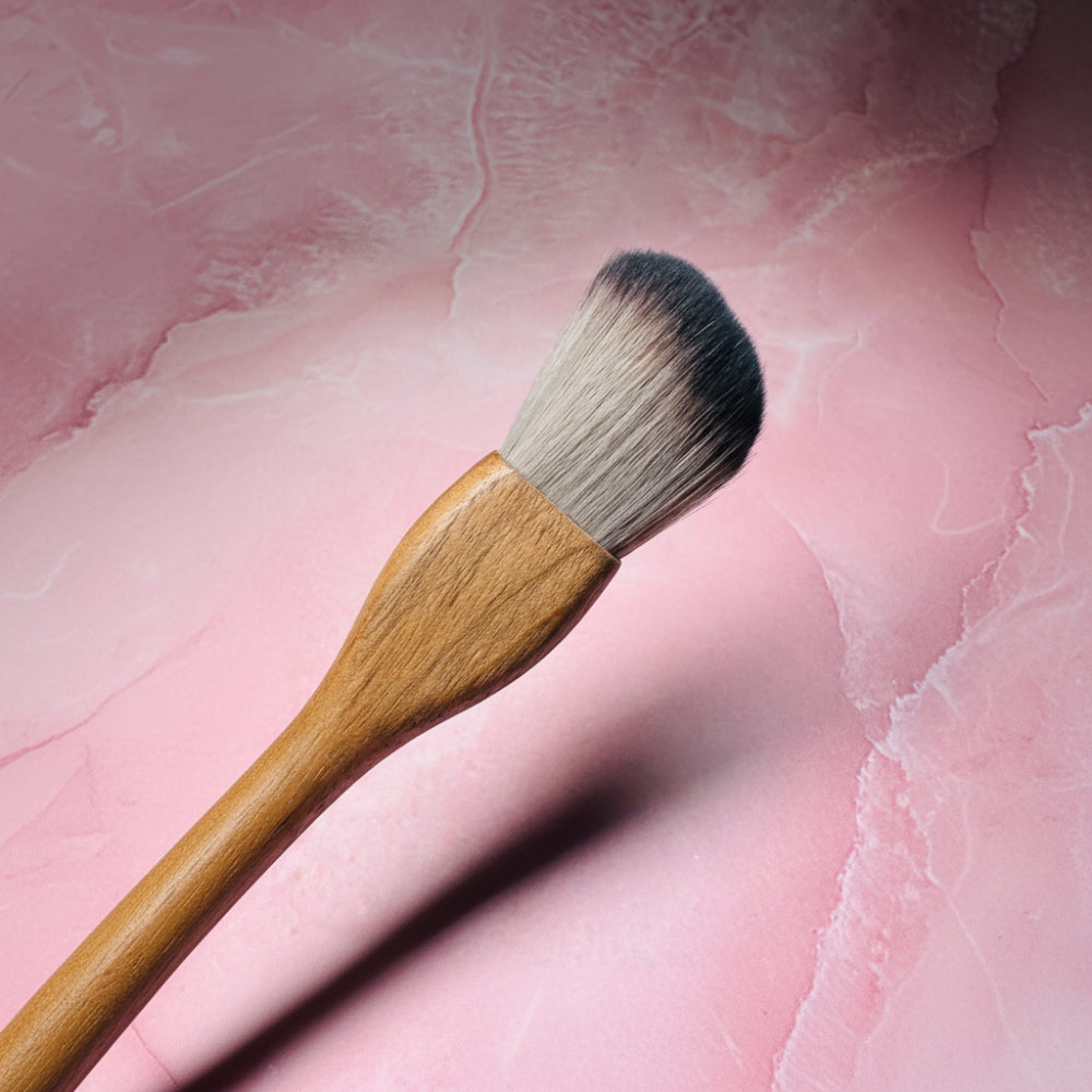Makeup brush with wooden handle on a pink textured background