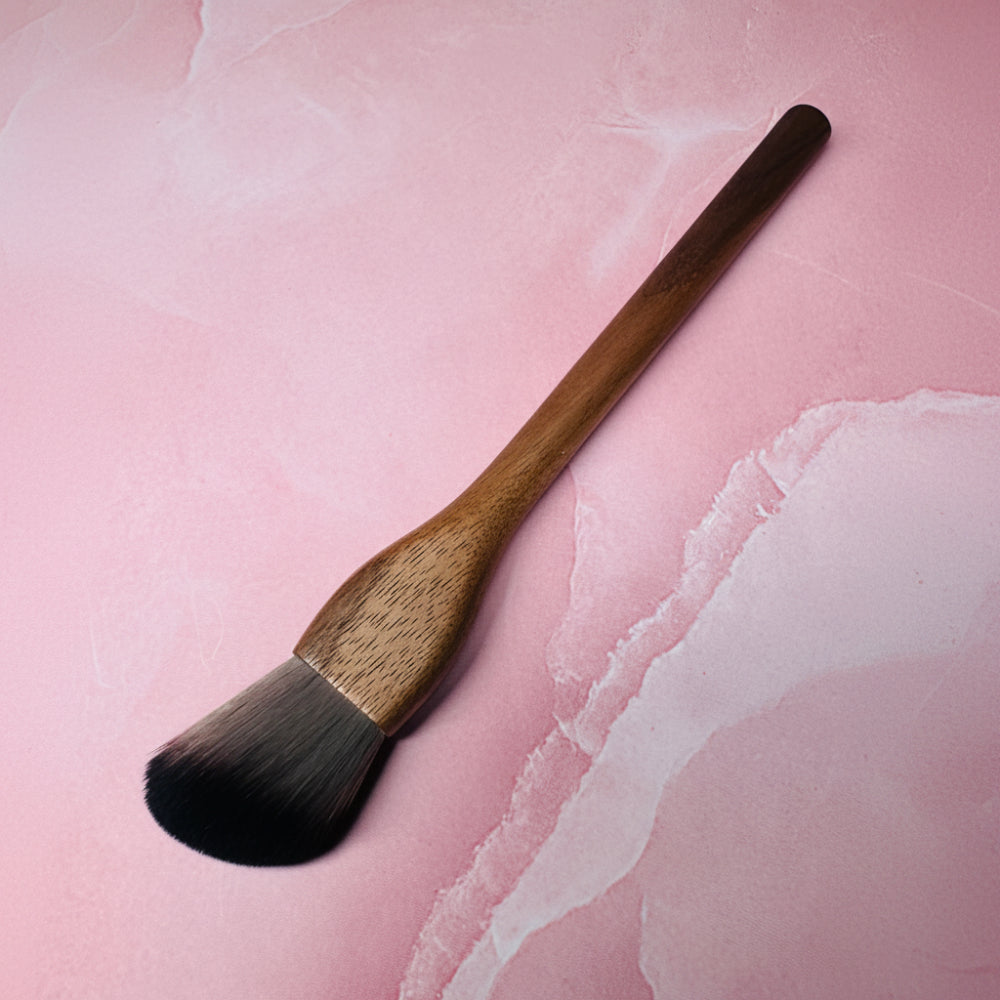Makeup brush with wooden handle on a pink textured background